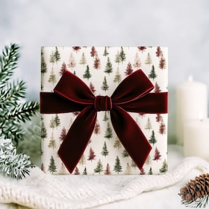 May include: A wrapped gift box with a festive design. The wrapping paper features a pattern of small evergreen trees in shades of green, brown, and beige. A wide, deep red velvet ribbon is tied around the box in a bow.