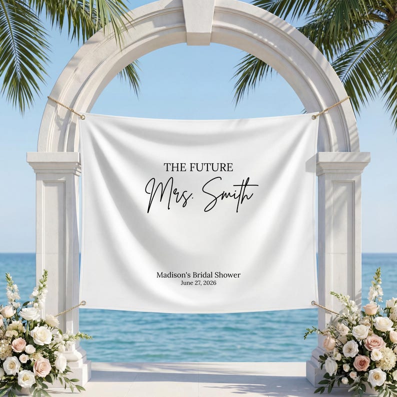 May include: A white banner with the text "THE FUTURE Mrs. Smith" in black script, displayed on a white archway. The banner also includes "Madison's Bridal Shower June 27, 2026". The scene is set by the ocean with floral arrangements.