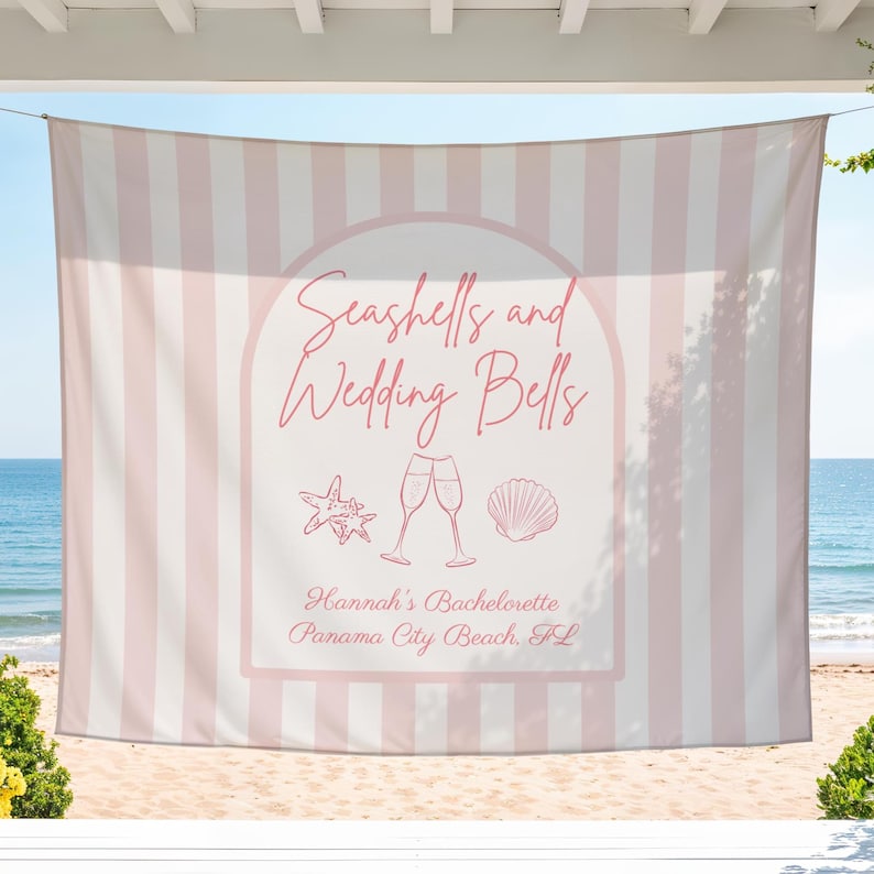 May include: A pink and white striped beach towel with the text "Seashells and Wedding Bells" in a decorative font. The towel features a seashell and champagne glass graphic, with the text "Hannah's Bachelorette Panama City Beach, FL".