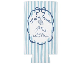May include: A light blue and white vertical striped can cooler featuring a dark blue ribbon frame graphic. Inside the frame is the text They're Engaged, a disco ball, an illustration of two hands, and the text Cheers to Julianna & Marco.
