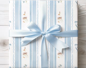 May include: A wrapped gift with light blue satin ribbon. The wrapping paper features a pattern of white geese with party hats and bows, set against a backdrop of vertical blue stripes and floral accents. The bow is tied on top of the gift.