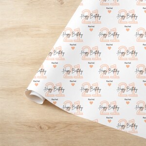 May include: White wrapping paper with a repeating pattern of peach-colored numbers "21" with the text "Happy Birthday" and the name "Rachel" repeated throughout.  There are also small peach-colored hearts.