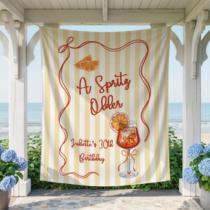 May include: A yellow and white striped banner with the text "A Spritz Older" in red script. The banner also features an illustration of an orange slice and a cocktail. The text "Juliette's 30th Birthday" is also on the banner.
