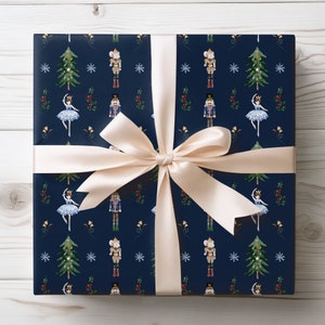 May include: A wrapped gift with navy blue wrapping paper featuring a repeating pattern of a ballerina, nutcracker, Christmas tree, mouse, and snowflakes. The gift is tied with a cream-colored satin ribbon and bow.