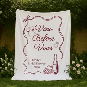 May include: White fabric banner with burgundy text and illustrations. The banner reads "Vino Before Vows" with wine glasses, a ring, a wine bottle, and grapes. It also includes "Emily's Bridal Shower 2026".