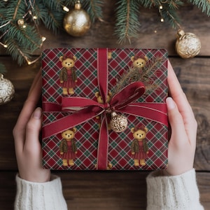 May include: A wrapped gift with a red plaid pattern featuring teddy bears in dresses. The gift is tied with a burgundy ribbon and a gold ornament. The background includes Christmas tree branches and gold ornaments.