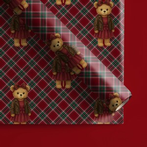 May include: Wrapping paper with a repeating pattern of teddy bears wearing red dresses and brown jackets. The background is a red, green, and white plaid design. The paper is partially rolled, revealing a solid red background.