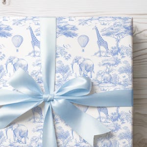 May include: A blue and white gift wrap with a pattern of giraffes, elephants, and hot air balloons. The gift wrap is tied with a light blue ribbon.