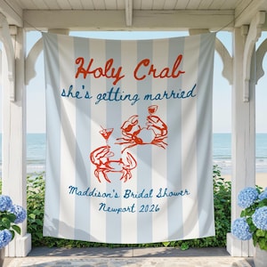 Könnte beinhalten: Ein vertikales Stoffbanner mit hellblauen und weißen vertikalen Streifen. Der Text lautet Holy Crab she's getting married, Maddison's Bridal Shower und Newport 2026. Zwei orangefarbene Krabbenillustrationen halten jeweils ein Getränk.
