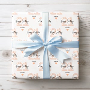 May include: White gift wrap with a light blue ribbon. The wrapping paper has a repeating pattern of the number 21 in peach with the text "Happy Birthday" and the name "Rachel".