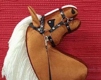 May include: A brown plush horse head with a white mane and tail. The horse has a black leather bridle with silver accents and a black leather rein.
