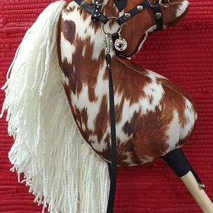 May include: A brown and white spotted rocking horse with a white mane and tail. The horse has a black leather bridle with silver accents and a silver charm.
