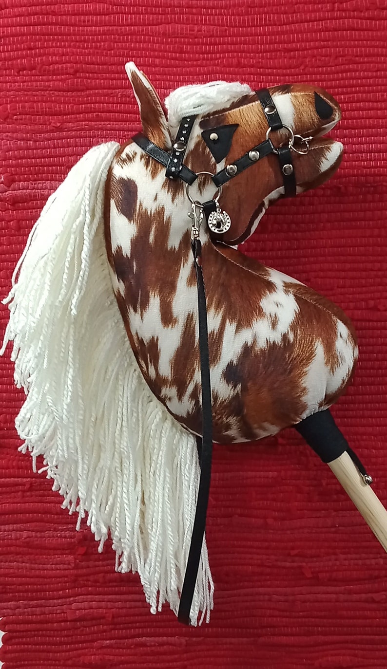 May include: A brown and white spotted rocking horse with a white mane and tail. The horse has a black leather bridle with silver accents and a silver charm.