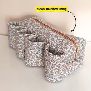 May include: A floral print organizer with multiple pockets and a copper zipper. The fabric has a light blue background with pink and brown flowers. The organizer has a clean-finished lining.