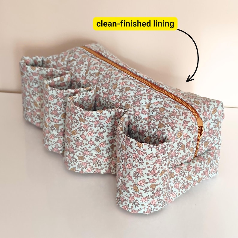 May include: A floral print organizer with multiple pockets and a copper zipper. The fabric has a light blue background with pink and brown flowers. The organizer has a clean-finished lining.