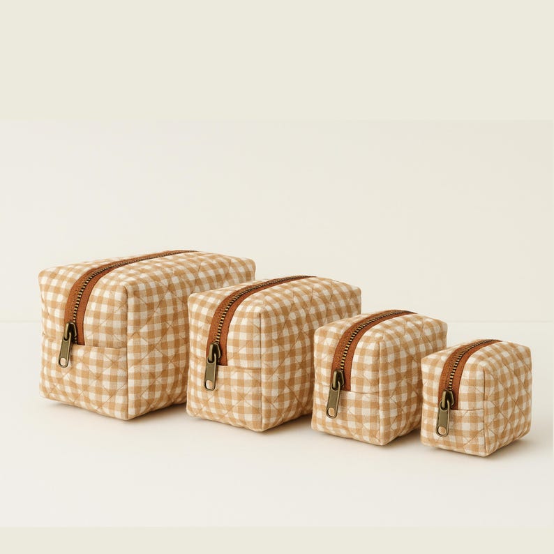 May include: Four beige and white gingham patterned cosmetic bags of varying sizes. Each bag has a brown zipper and a quilted design. The bags are arranged in a row, with the largest on the left and smallest on the right.