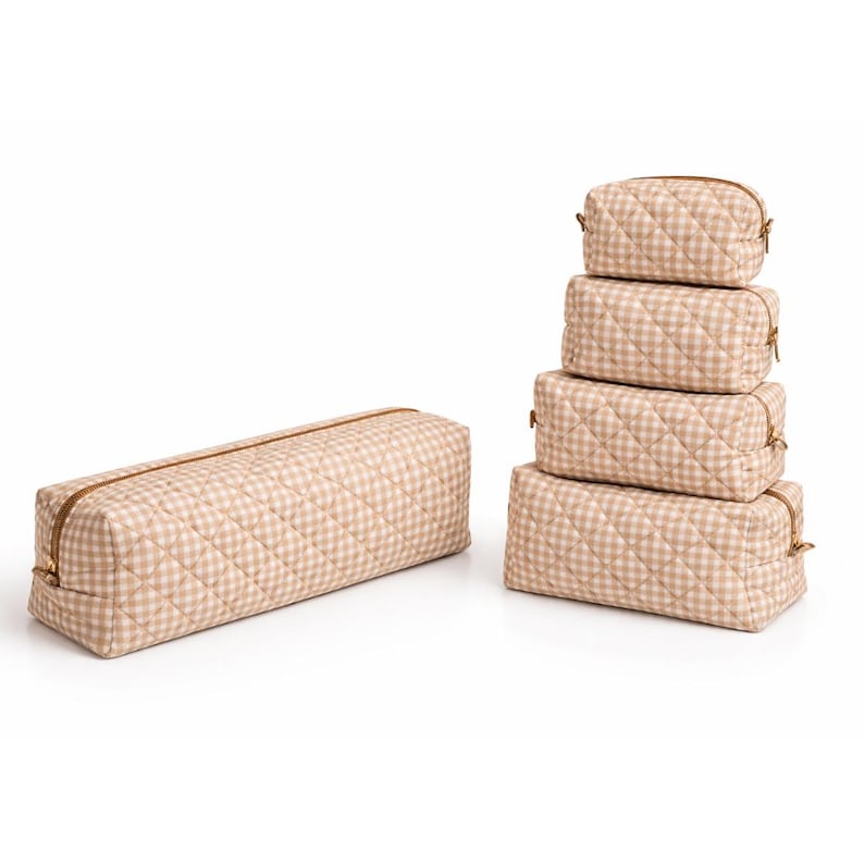 May include: A set of five beige and white gingham patterned cosmetic bags in various sizes. The bags are quilted and have gold-colored zippers. One long rectangular bag is separate from the stack of four smaller bags.