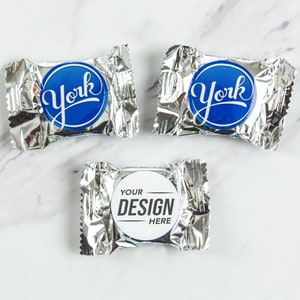 May include: Three silver foil-wrapped chocolate candies. Two candies have a blue circle with the word "York" in white. The third candy has a white circle with the text "Your Design Here" in black.