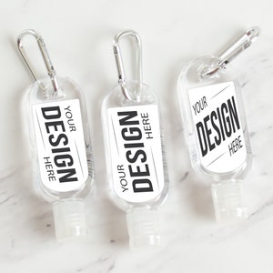 May include: Three clear plastic hand sanitizer bottles with a carabiner clip. Each bottle has a white label with black text that reads "YOUR DESIGN HERE".