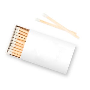 May include: A white matchbox filled with wooden matches, each with a white tip. Two matches are placed on top of the box. The matches are a light brown color.