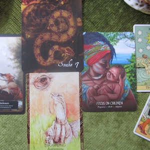 May include: A tarot card reading spread with ten cards laid out on a green surface. The cards include "The Star", "8 of Pentacles", "Focus on Children", "6. Trusting Tricksters", "Snake 7", and "Drawing Authenticity".