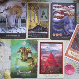 May include: A spread of ten tarot cards, including the Six of Swords, Six of Pentacles, Frog Spirit, Sit With Your Soul, and Gray Squirrel. The cards are laid out on a floral patterned fabric.