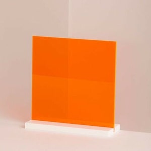 May include: A bright orange acrylic sheet standing on a white base. The sheet is translucent and has a smooth surface.