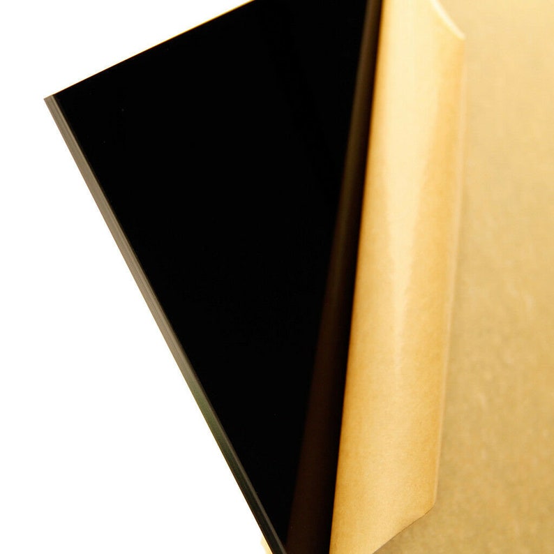 Puede incluir: Primer plano de una l&aacute;mina de acr&iacute;lico negro con un respaldo de papel protector. La l&aacute;mina es lisa y reflectante.
