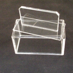May include: A clear acrylic box with a hinged lid. The lid is open and the box is empty.