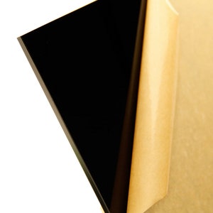 May include: A sheet of black acrylic with a protective paper backing. The paper is partially peeled back to reveal the smooth, glossy surface of the acrylic.