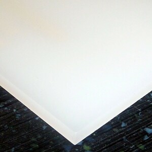 May include: A close-up of a white cutting board with a slightly rounded edge. The board is made of a smooth, non-porous material.