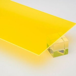 May include: A bright yellow sheet of acrylic plastic, shown on a white surface. The acrylic sheet is resting on a clear glass block.