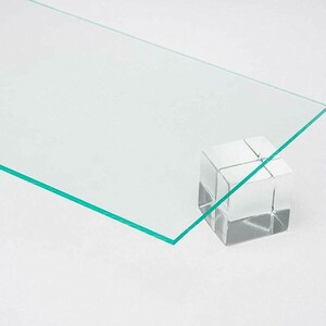 May include: A clear, rectangular sheet of acrylic plastic with a green edge. The sheet is resting on a clear acrylic block.