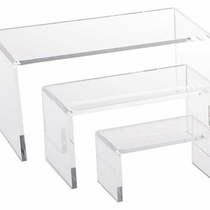 May include: Set of three clear acrylic risers, each with a different height. The risers are made of sturdy acrylic and are perfect for displaying products or showcasing items in a retail setting.