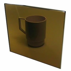 May include: A brown ceramic mug with a handle reflected in a gold mirror.