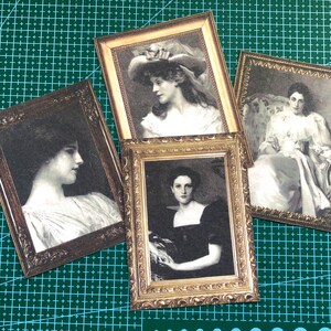 Puede incluir: Cuatro marcos dorados ornamentados con retratos de mujeres con ropa vintage. Cada marco tiene un dise&ntilde;o diferente y presenta a una mujer con un peinado y una expresi&oacute;n diferentes.