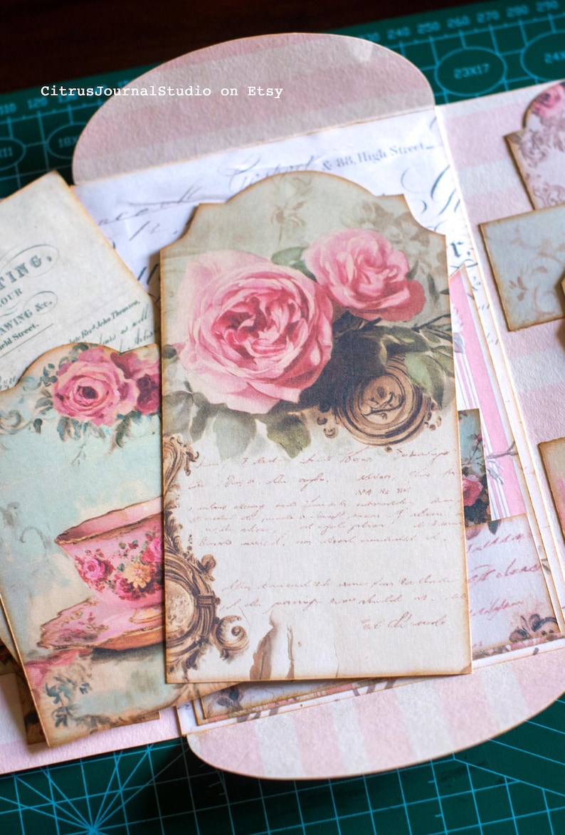 Pu&ograve; includere: Una collezione di efemeridi di carta in stile vintage con un tema rosa e floreale. Il punto focale &egrave; un'etichetta con rose rosa, scritte e un orologio decorativo. Altri elementi includono un'illustrazione di tazza da t&egrave; e il testo "CitrusJournalStudio on Etsy."