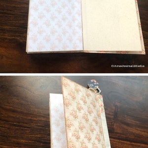 May include: A closed journal with a floral patterned cover. The journal has a brown paper cover with a floral pattern in pink and green. The journal is closed and has a tag attached to it that says "80 pages".