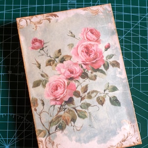 Pu&ograve; includere: Una copertina di diario rettangolare con un design floreale vintage. Mostra un bouquet di rose rosa con foglie verdi su uno sfondo azzurro. Il testo "CitrusJournalStudio on Etsy" &egrave; visibile.