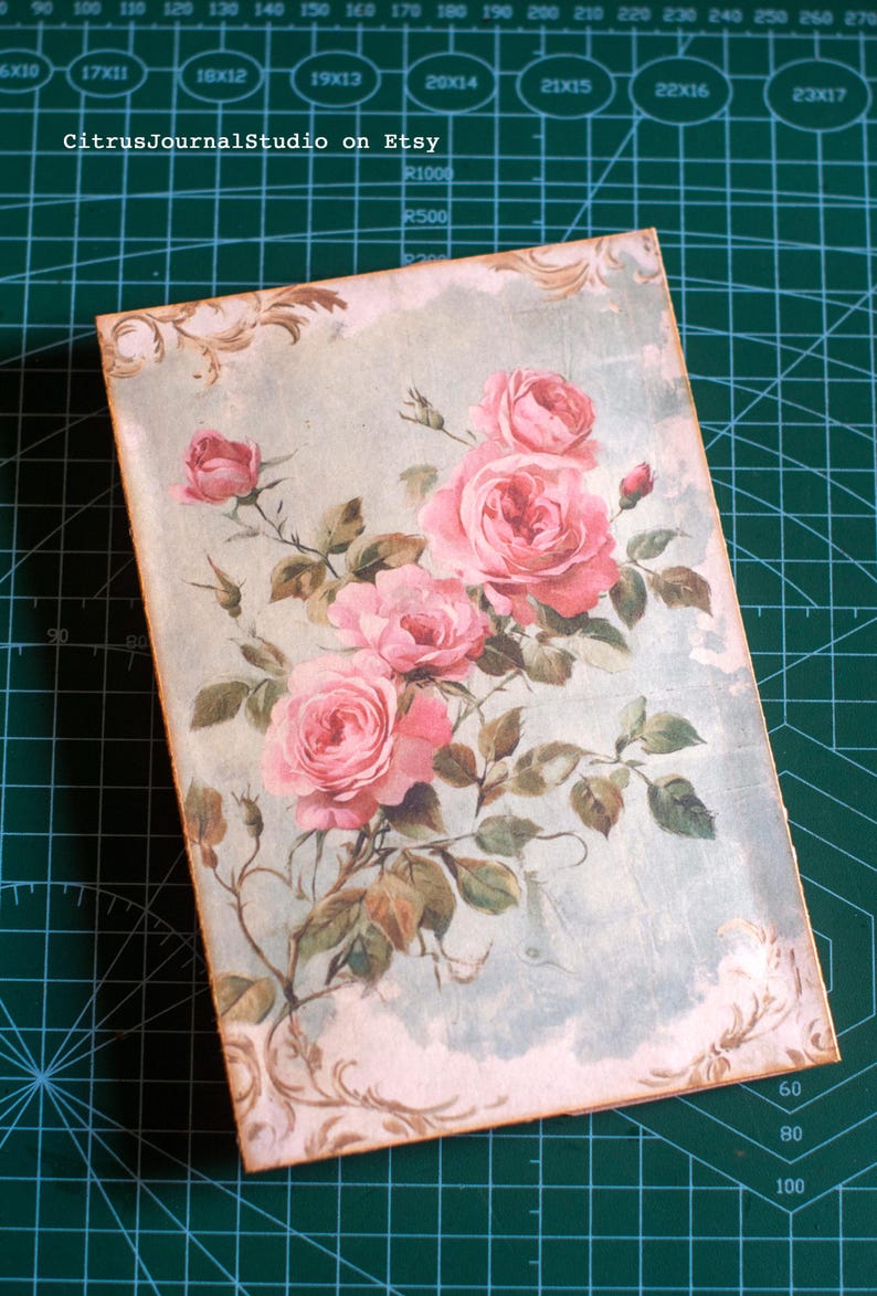 Pu&ograve; includere: Una copertina di diario rettangolare con un design floreale vintage. Mostra un bouquet di rose rosa con foglie verdi su uno sfondo azzurro. Il testo "CitrusJournalStudio on Etsy" &egrave; visibile.