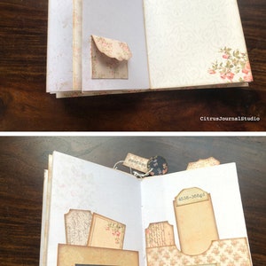 May include: An open journal with a floral design on the cover. The pages are decorated with vintage-style paper ephemera, including tags, labels, and pockets. The text on the page reads "REES DE LA PRATIQUE 'ur les Playıs d'armes &agrave; fru." and "Rungis Market March&eacute; pour Eleveur".