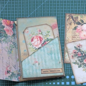 Könnte beinhalten: Ein Scrapbook mit floralem Design und dem Schriftzug "make memories" auf der Vorderseite. Das Scrapbook hat eine Tasche auf der Vorderseite und ist mit mehreren floral gemusterten Papieren verziert.