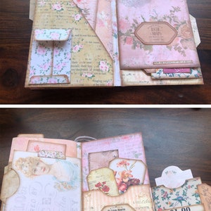 May include: An open scrapbook with a pink and white floral theme. The scrapbook has several pockets and tabs, and is decorated with various paper embellishments, including a tag that reads "Bath Soap".