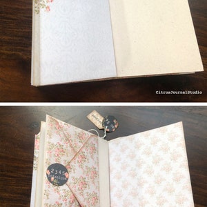 May include: Open journal with floral patterned pages. The left page has a floral envelope with a black circle sticker that says "2345 botanique". The right page has a floral pattern. The top of the journal has a tag that says "no 84" and another tag that says "French Garden Treasures - Everything for your garden".
