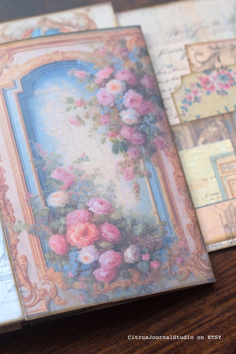 May include: A vintage-style journal cover with a floral design. The cover features a gold frame with a blue and white background and a bouquet of pink and white roses.