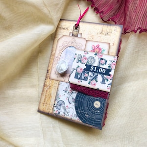 Puede incluir: Un diario de estilo vintage con un diseño floral y una etiqueta de precio que dice "1,00 €". El diario está decorado con un borde de encaje y una pequeña flor blanca.