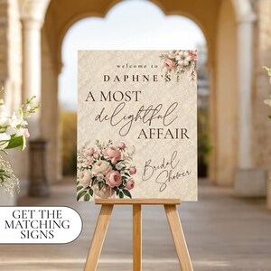 May include: A decorative sign on a wooden easel, featuring the text "Welcome to Daphne's, A Most Delightful Affair, Bridal Shower." The sign has floral accents in pink and white. The words "Get the matching signs" are in a white oval.