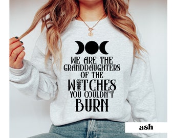 Może przedstawiać: Szara bluza z nadrukiem "We are the granddaughters of the witches you couldn't burn" w kolorze czarnym. Tekst jest otoczony symbolem potrójnego księżyca. Bluza jest oznaczona jako "ash".