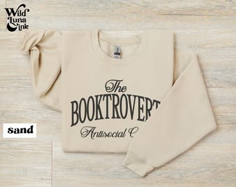 Op de afbeelding: Een beige sweatshirt met de tekst "The Booktrovert Antisocial Club" gedrukt op de voorkant.