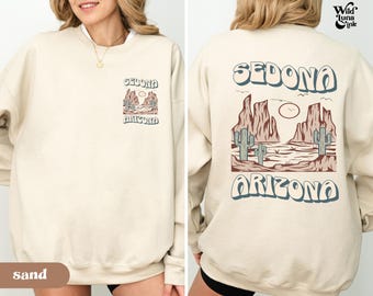 May include: A beige sweatshirt with a graphic print of a desert landscape with the text "SEDONA ARIZONA" on the back and "SEDONA ARIZONA" on the front. The sweatshirt is made of a soft, comfortable material and is perfect for everyday wear.